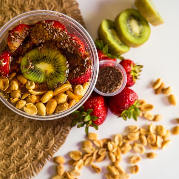 Overhead view of an acai bowl with strawberries, kiwi, peanuts, and flax seeds on a burlap mat.