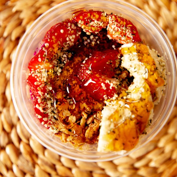 Overhead view of an acai bowl with strawberries, granola, and honey in a clear plastic container.
