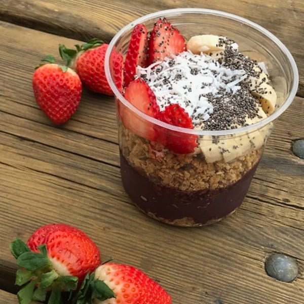 Acai bowl with strawberries, bananas, granola, shredded coconut, and chia seeds on a wooden table.