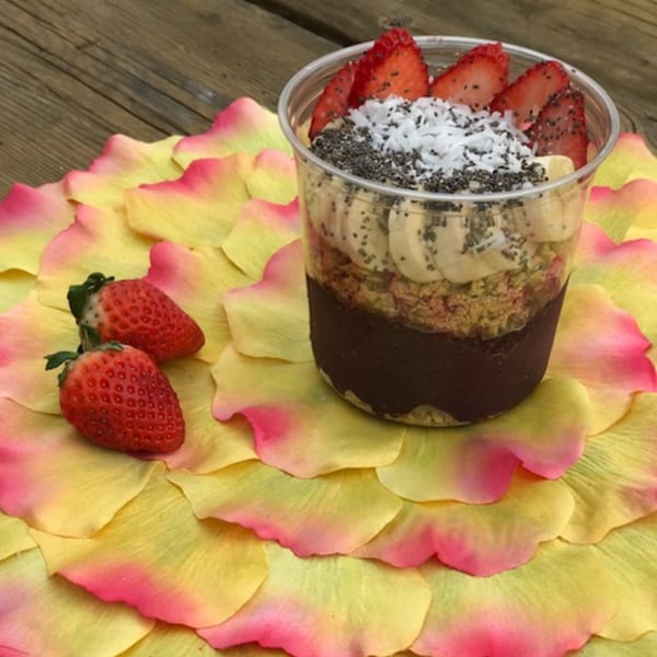 An acai bowl with strawberries, bananas, coconut, and chia seeds on a bed of yellow and pink petals.