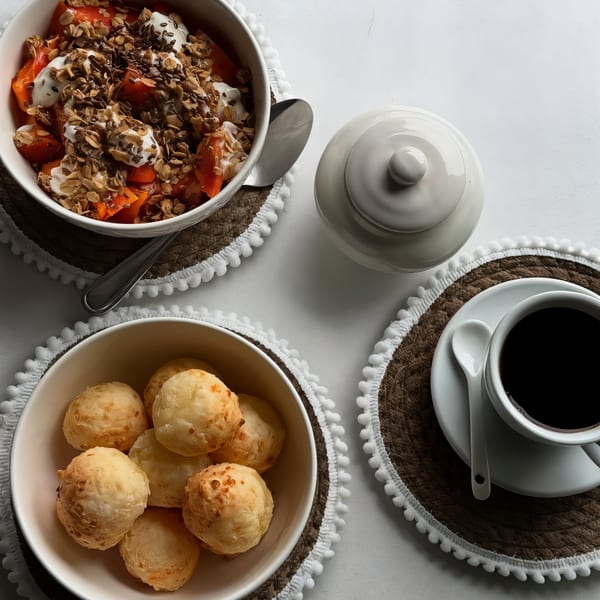 Overhead view of an acai bowl, cheese bread, and coffee on a white table with woven placemats.