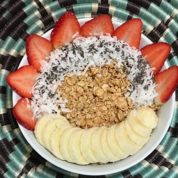 Acai bowl topped with sliced strawberries, bananas, shredded coconut, chia seeds, and granola.