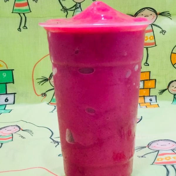 A vibrant pink acai smoothie in a clear plastic cup with a domed lid, against a playful green background.